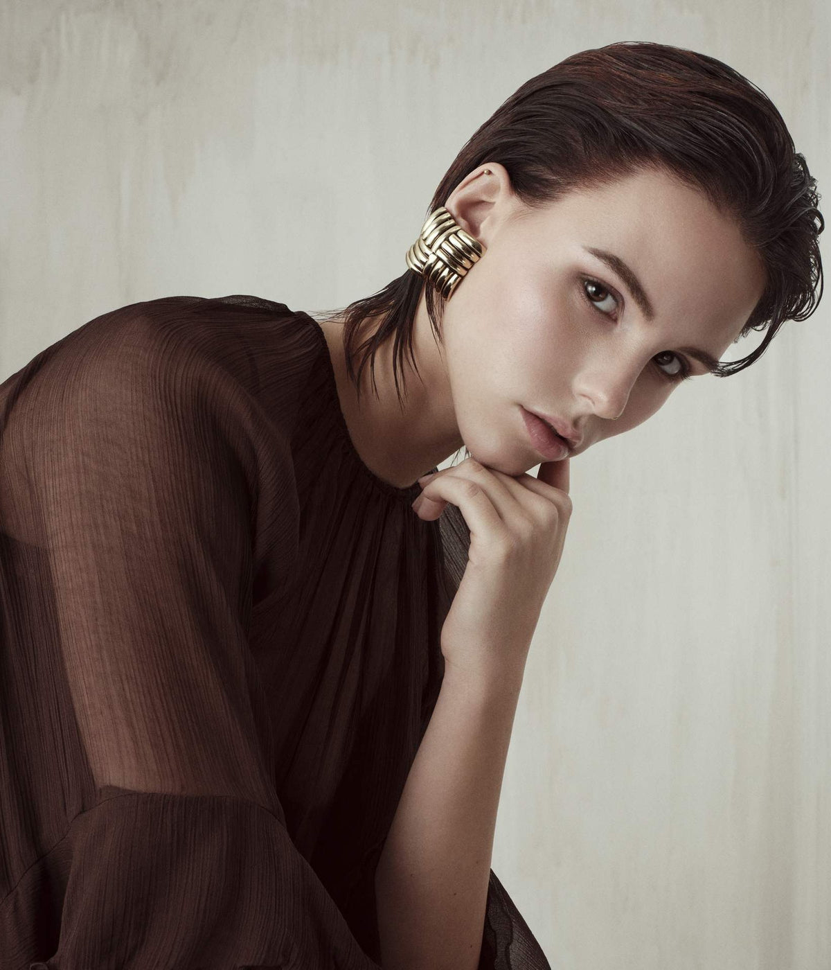 Modelo de cabello corto castaño oscuro peinado hacia atrás, con arete dorado y blusa café, colección People 2026 de Framesi