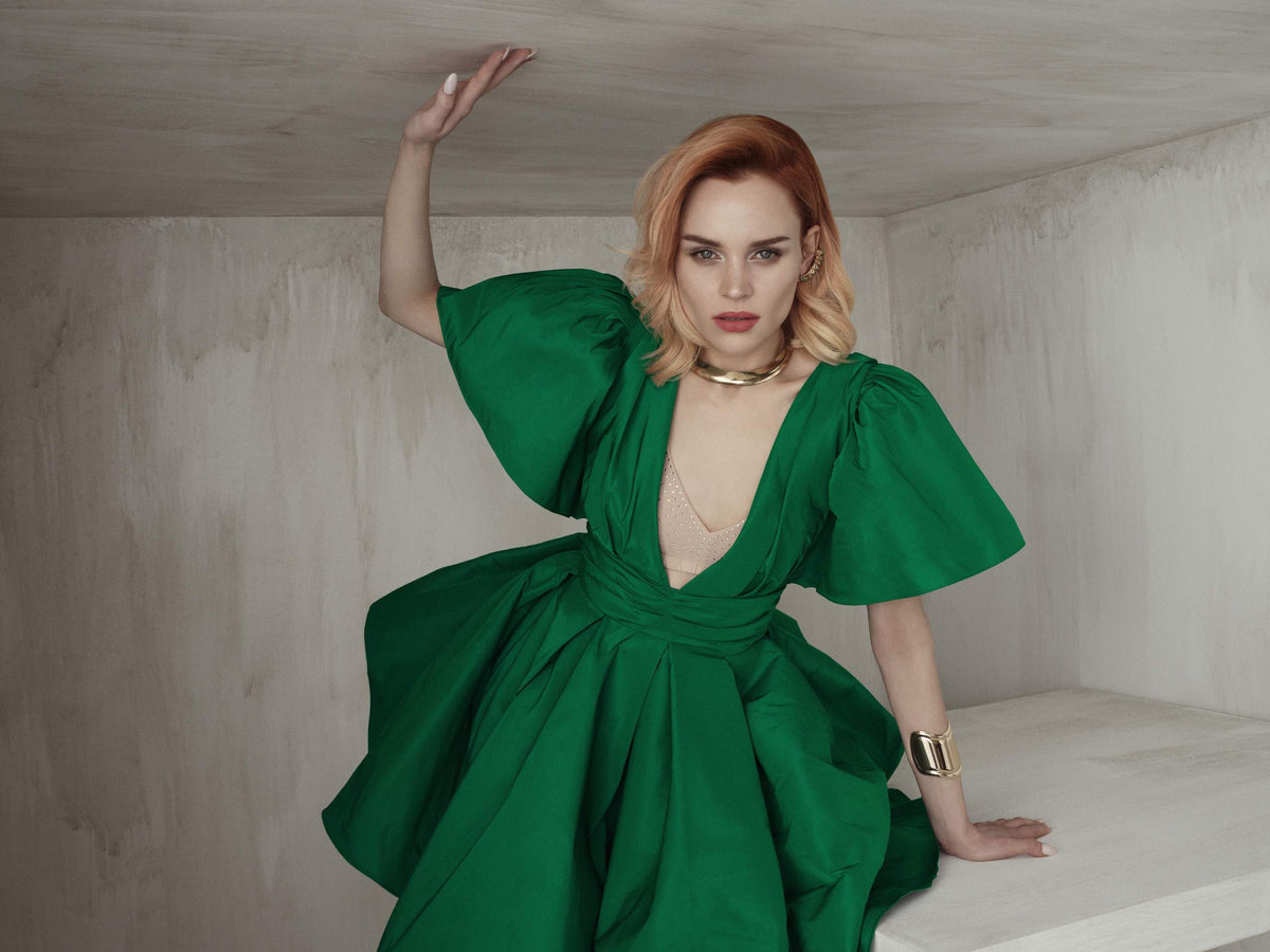 Modelo pelirroja con vestido verde escultural sentada en un set de concreto, colección People 2026 de Framesi