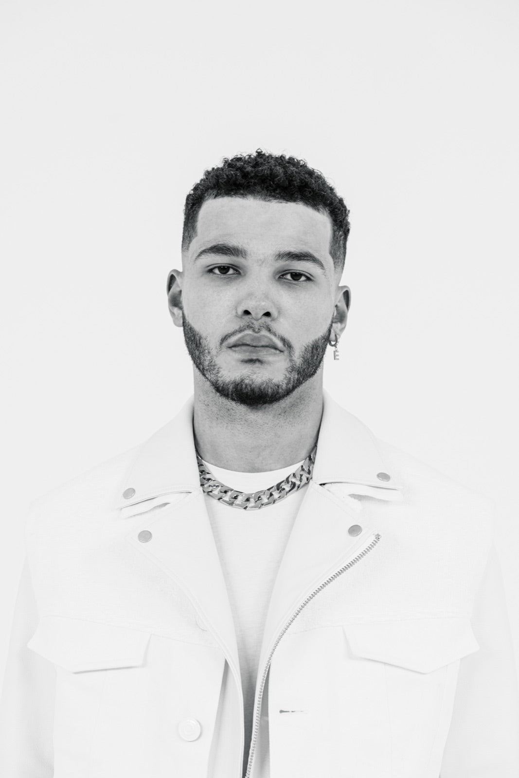 Hombre con corte fade y barba perfilada con chaqueta blanca, fotografía en blanco y negro