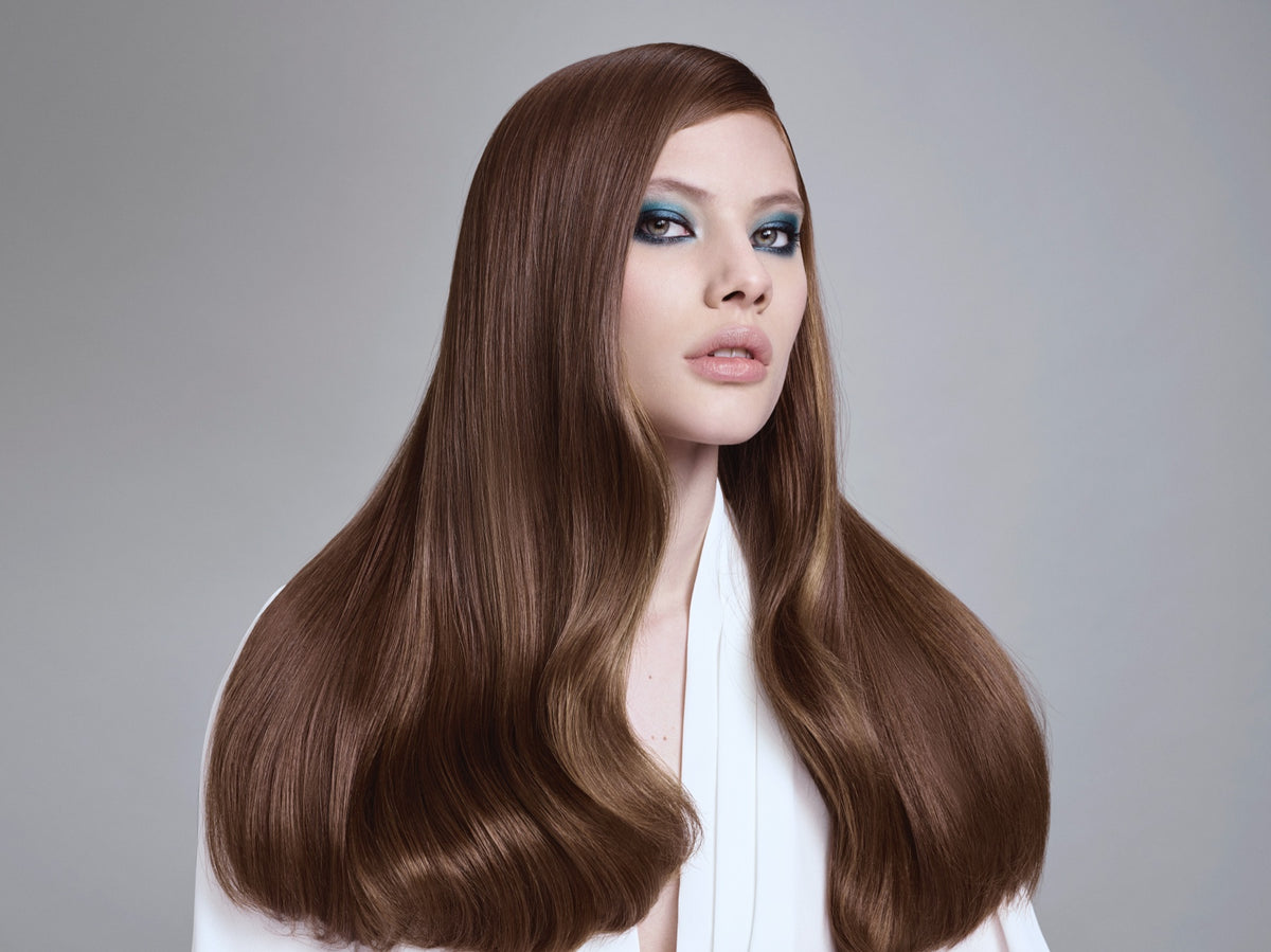 Modelo con cabello largo castaño liso y brillante sobre fondo gris